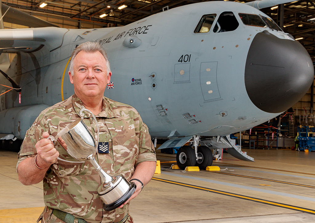 Chief Technician Craven standing in front of an Atlas (A400M), holding his trophy, received after being personally recognised with the Royal Air Force Association Liaison Officer (RAFALO) of the Year Award, acknowledging his exceptional contribution to the Association throughout 2024.
